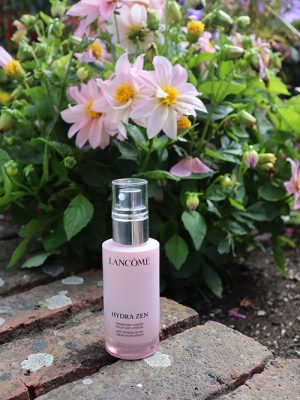 Image of Lancome bottle in front of greenery and pink flowers