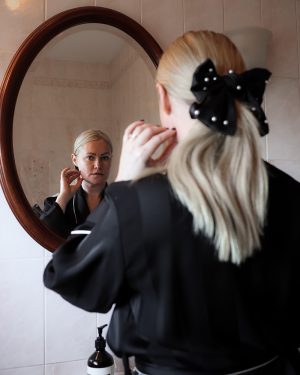 Image of Lorna Weightman looking into a mirror wearing a black robe and bow in a ponytail