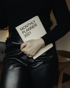 Image shows Lorna Weightman wearing a black outfit holding a notebook that is titled Monthly planner 2021