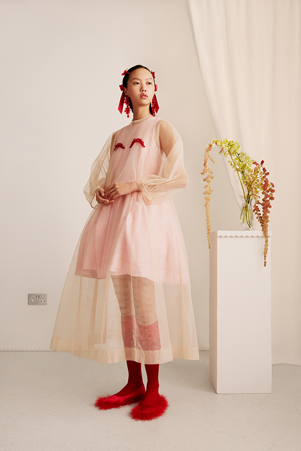 Image of female standing wearing cream tulle dress with red decoration and red socks and shoes